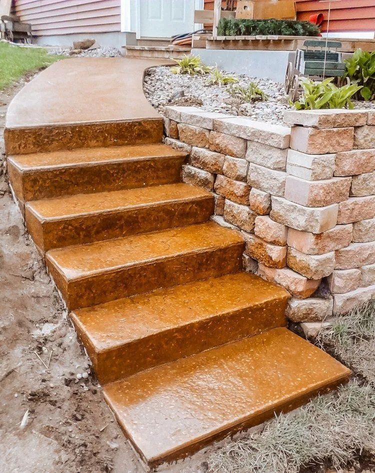 Concrete steps with a curved pathway leading up to a beige brick retaining wall.