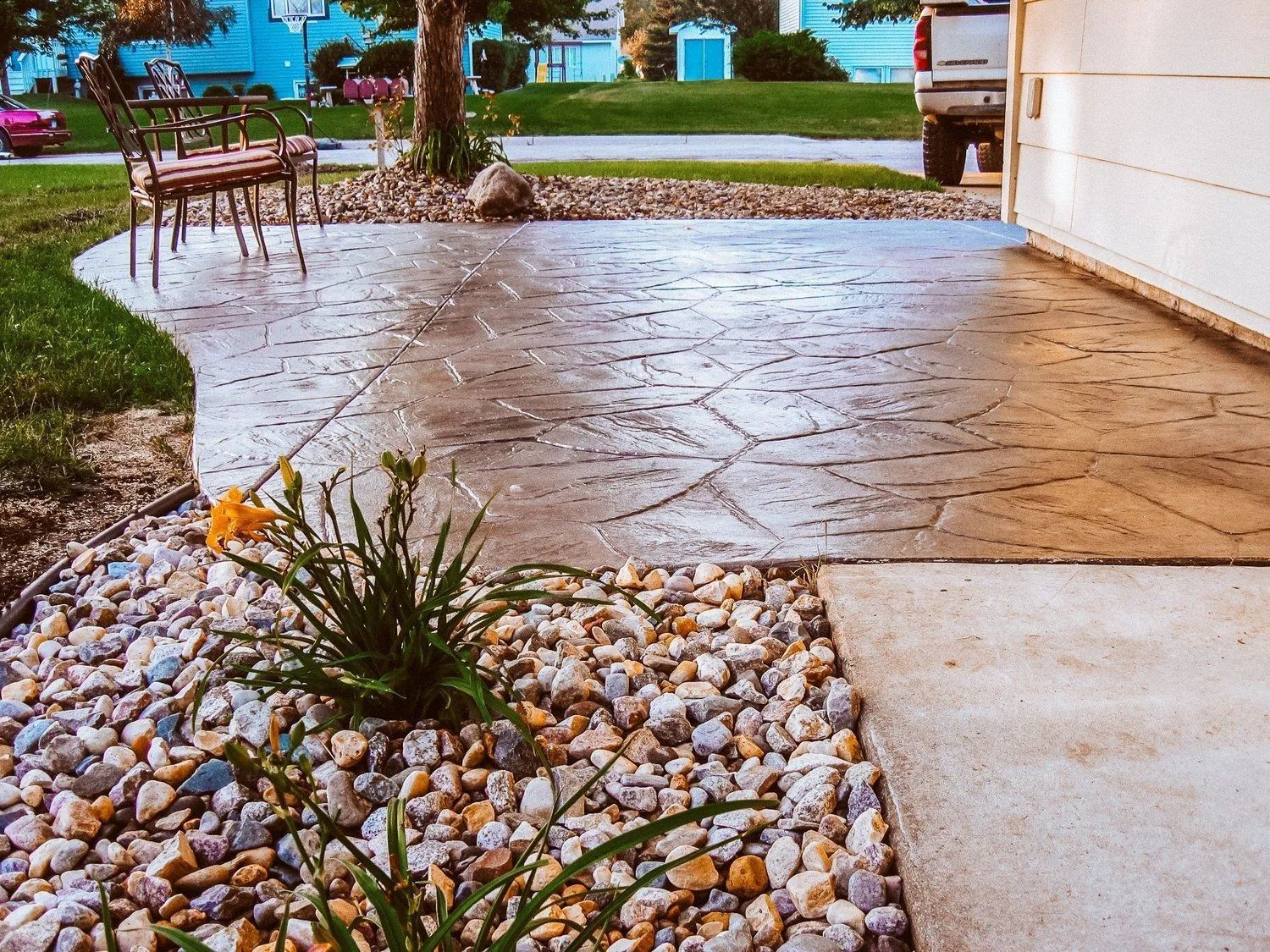 Stamped concrete patio with rock landscaping, chair, and driveway.