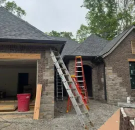 Two ladders against a brick house under construction, with a red bin and gravel driveway.