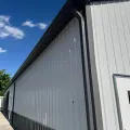 Long white metal-sided building with a sloped roof beside a gravel path under a blue sky.