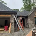 Two ladders against a brick house under construction, with a red bin and gravel driveway.