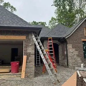 Two ladders against a brick house under construction, with a red bin and gravel driveway.