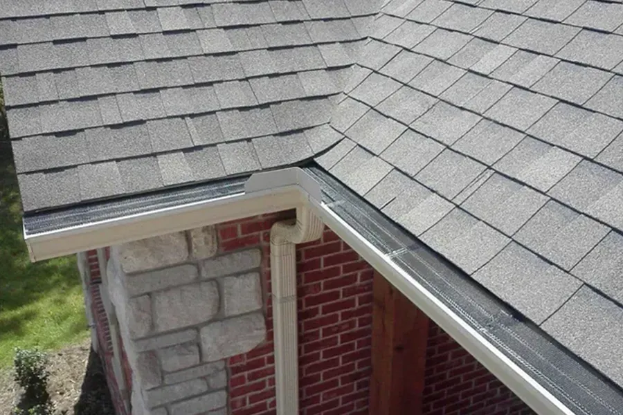 Roof valley and gutter detail on a house with gray shingles and stone-and-brick wall below