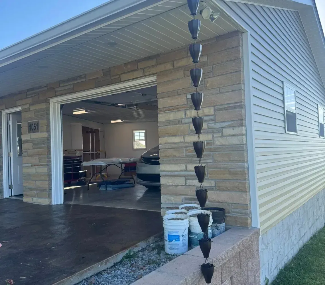 Open garage with a parked car and paint supplies beside the steps on the exterior wall