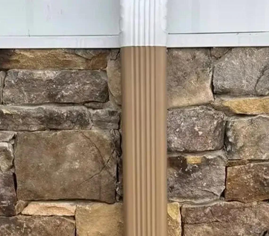 Stone veneer wall with white siding above and a dirt trench at the base, showing a vertical pipe in the center