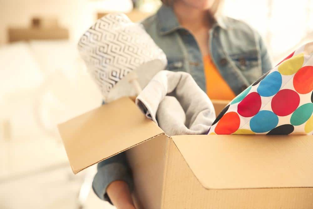 Woman is Holding a Cardboard Box Filled With Clothes — Bargara Removals in Rubyanna, QLD Woman is Holding a Cardboard Box Filled With Clothes — Bargara Removals in Rubyanna, QLD