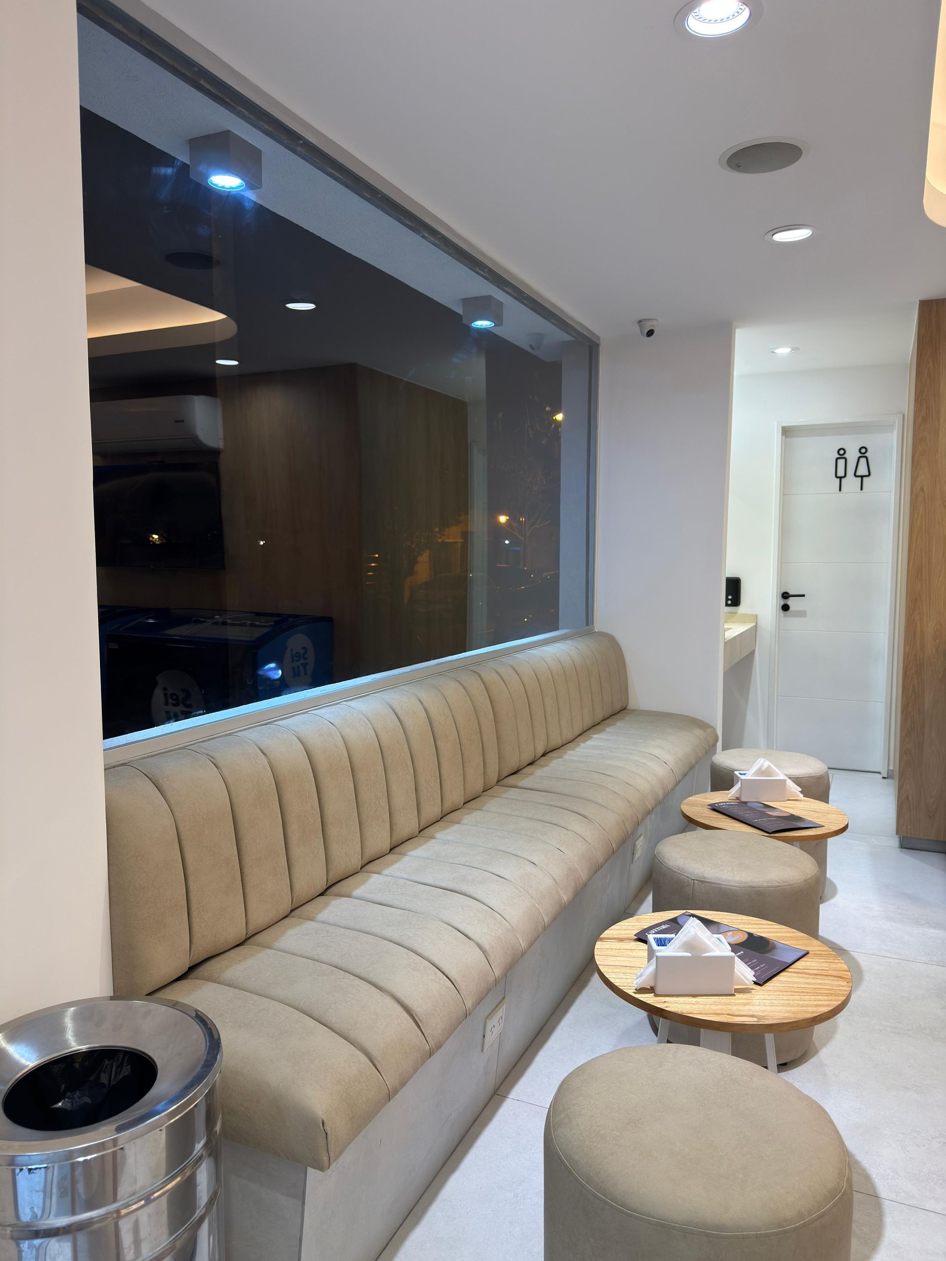 Salón moderno con un largo sofá beige, mesas auxiliares redondas y una ventana con vistas a la noche.