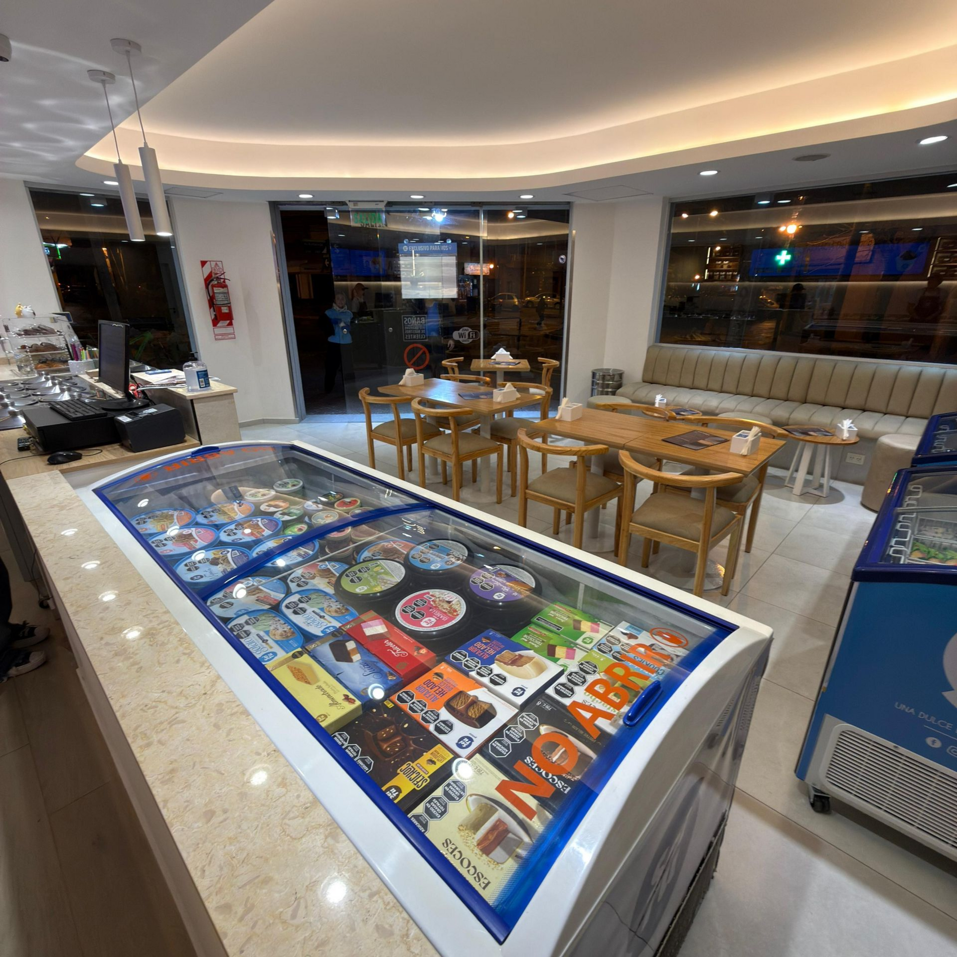 Restaurante moderno con mesas de madera y una vitrina con tapa de cristal en primer plano.