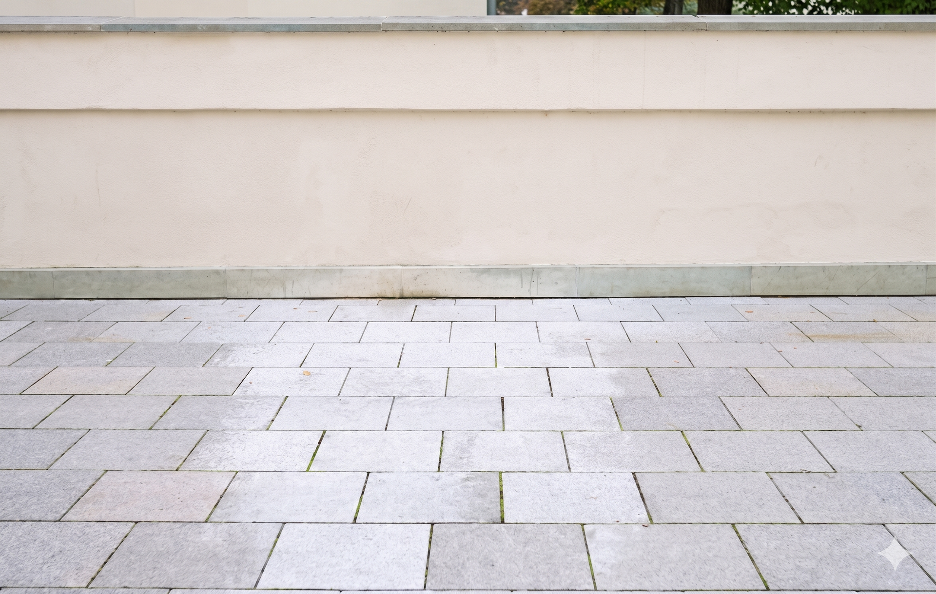 Empty stone-paved courtyard beside a beige wall with a narrow strip of grass at the top