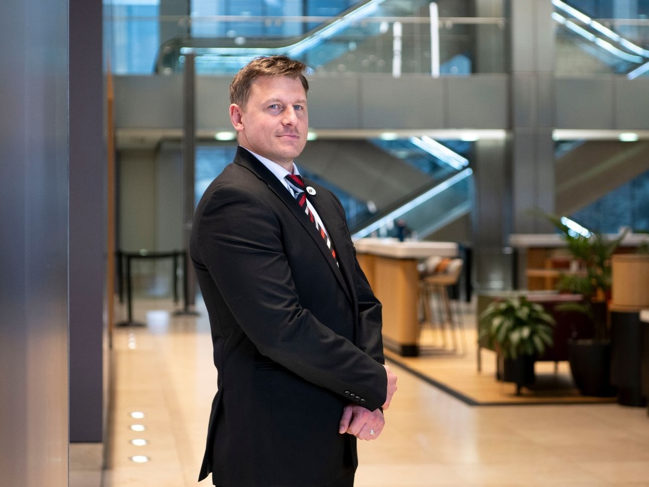 A person in a suit monitors a digital map of the UK and security camera feeds on a curved screen in a dim office.
