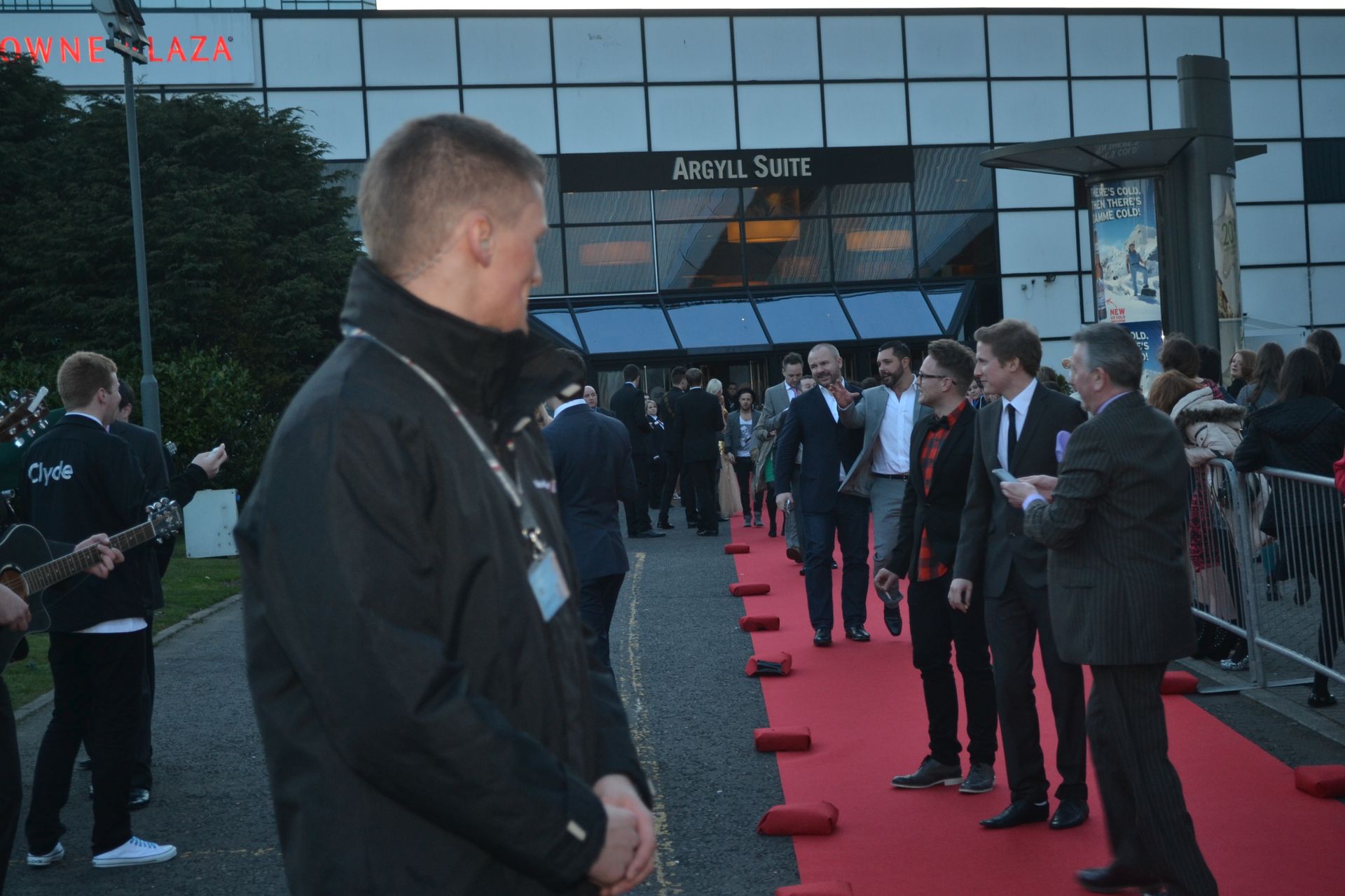 A person in a suit stands next to a woman in a suit by a Rolls-Royce parked on an airport tarmac near a private jet.