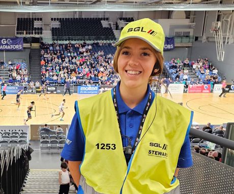 A staff member in a high-visibility vest stands in front of a blue UCI branded structure at an outdoor cycling event.