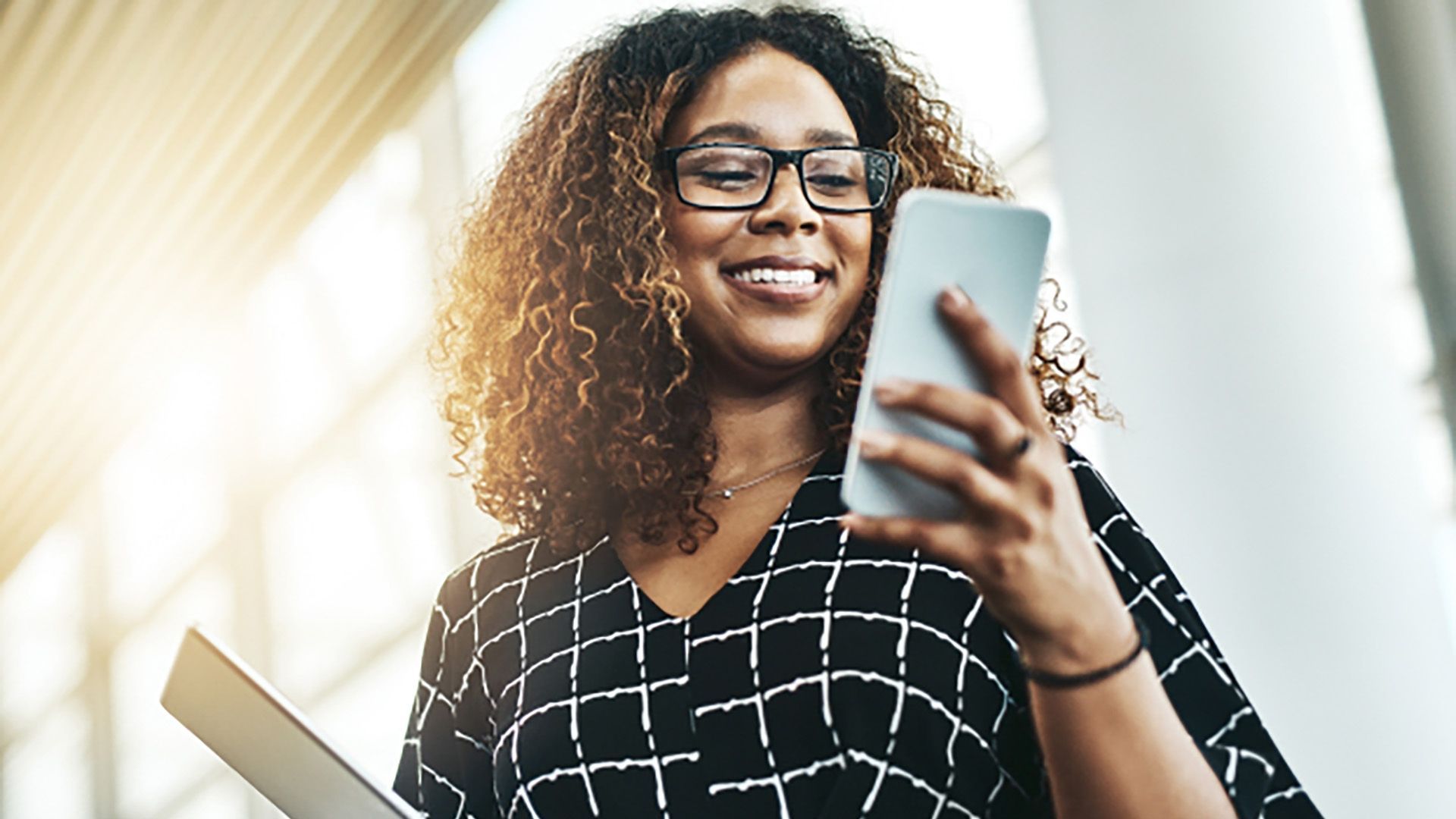 A woman wearing glasses is holding a tablet and a cell phone.