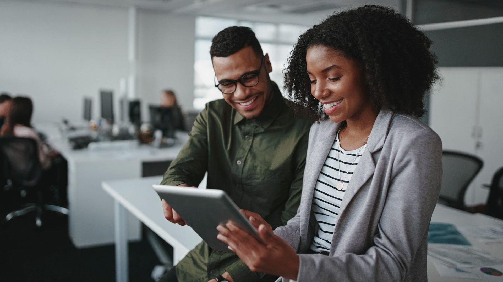 Un homme et une femme regardent une tablette ensemble dans un bureau.