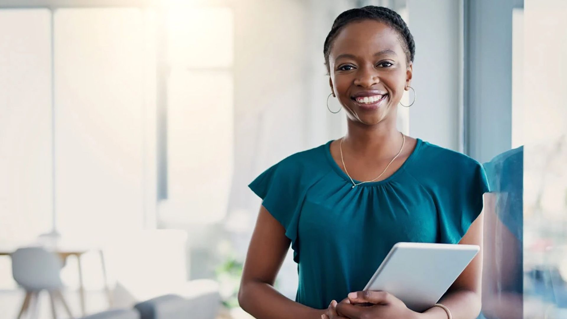 A woman in a blue shirt is holding a tablet and smiling.