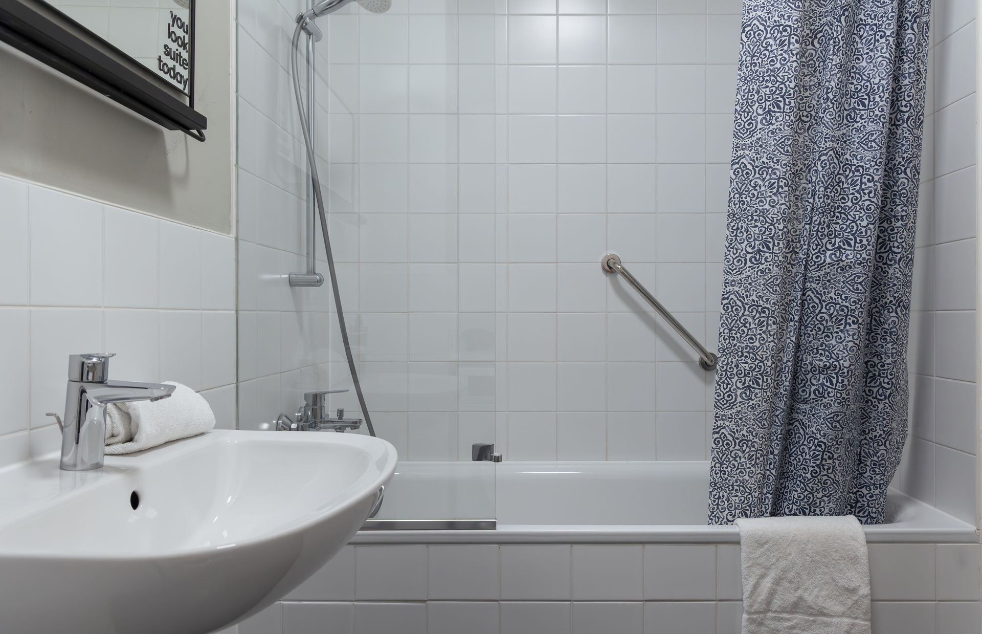 Small white tiled bathroom with pedestal sink, shower with shower screen, and bathtub.