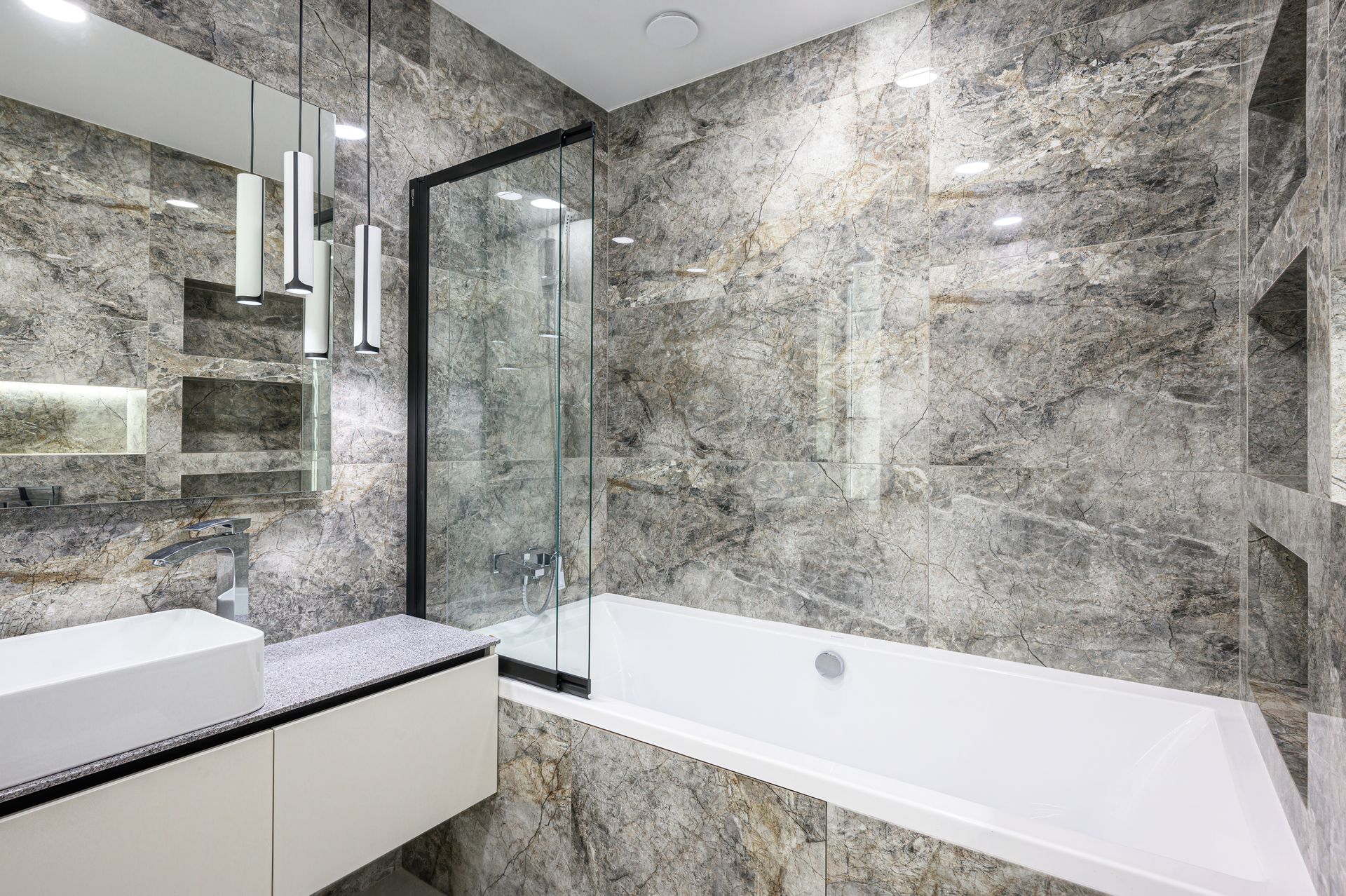 Modern luxury bathroom with marble walls, glass shower with shower screen, and white bathtub.
