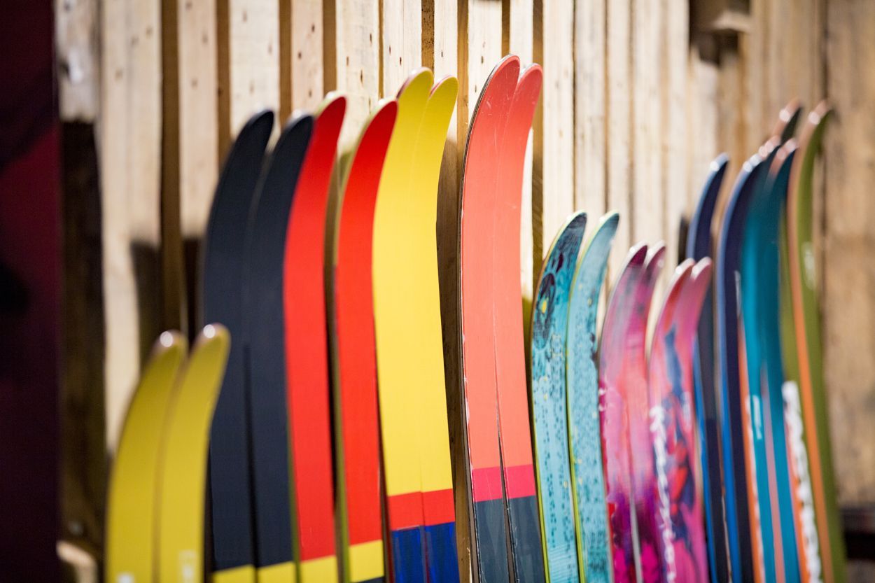 Plusieurs paires de skis allignées sur un muret de bois.