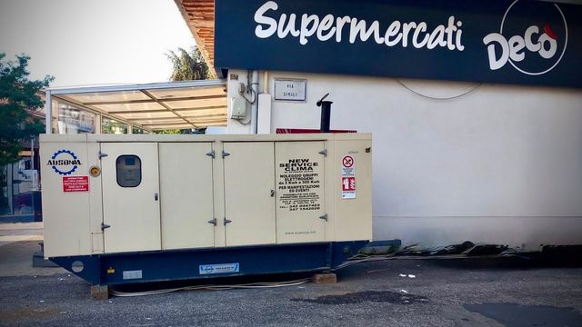 Grande camion generatore beige parcheggiato accanto a un edificio con l’insegna «Supermercati Deco».