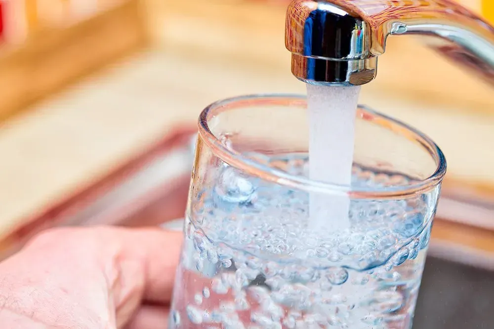 A person is pouring water into a glass from a faucet.