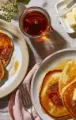 Pancakes with butter and syrup on plates, with a glass of juice on a breakfast table.