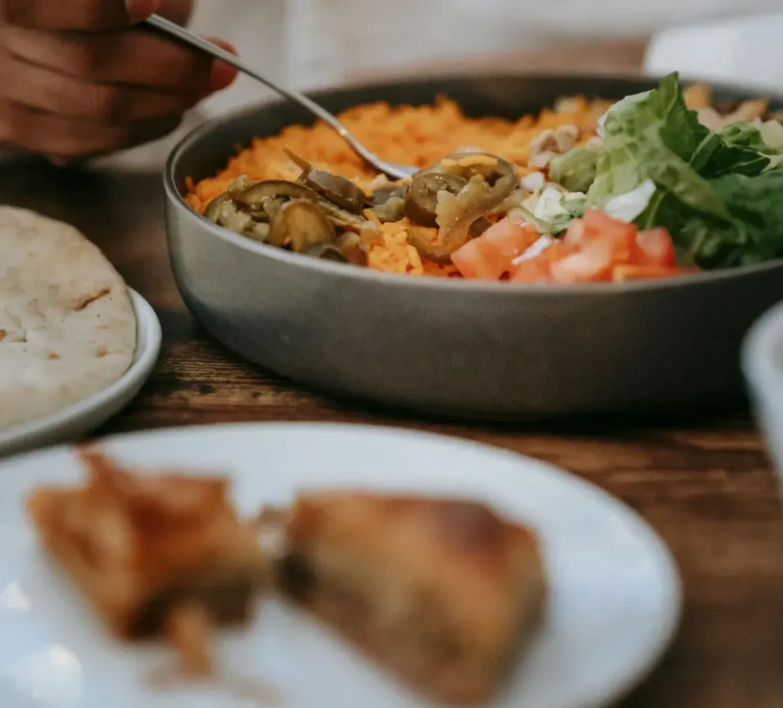 Person eating a rice bowl with greens and salmon at a table, with bread and a fork nearby