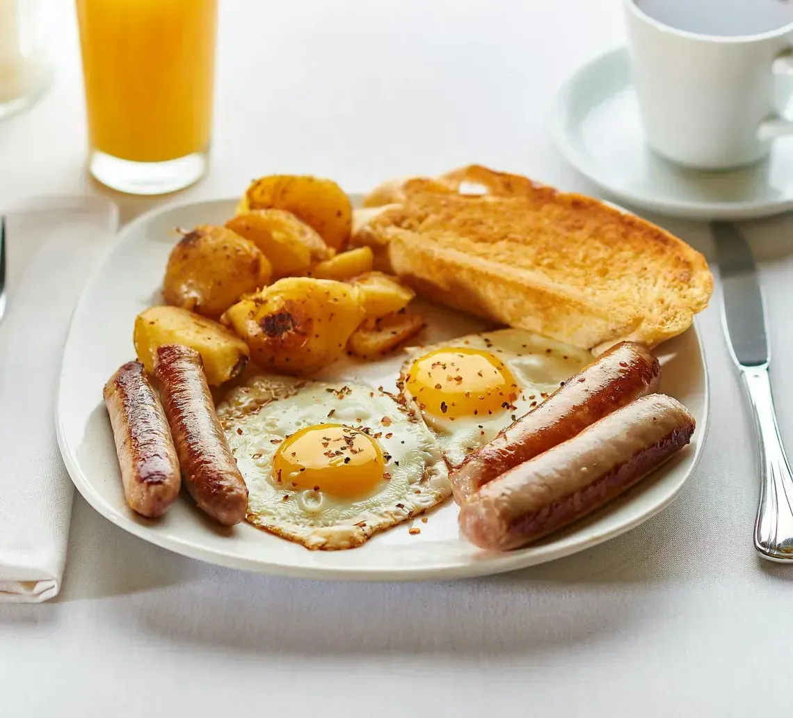 Breakfast plate with eggs, sausage, potatoes, and toast on a white table