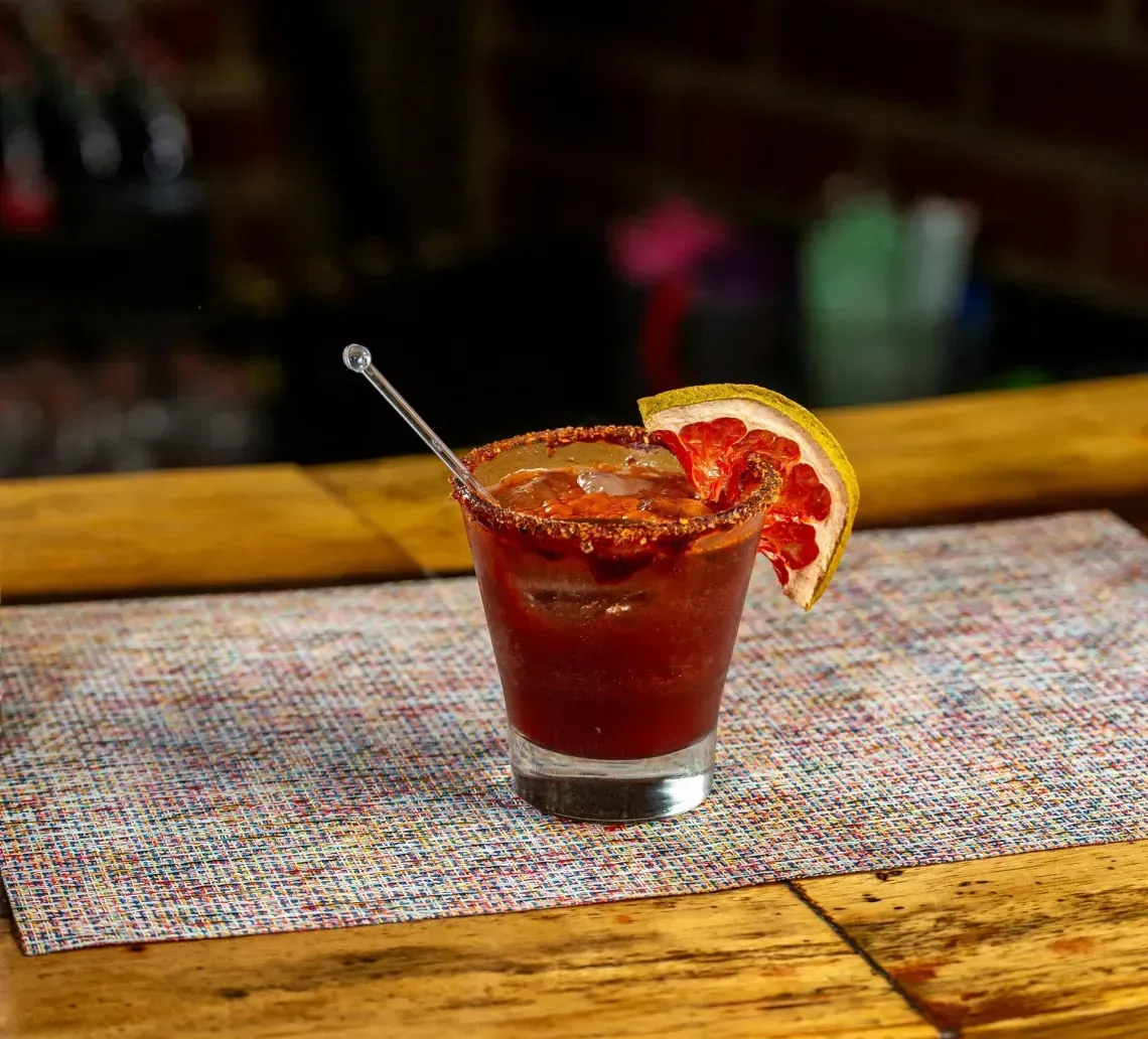A red cocktail in a glass with a citrus garnish on a bar counter