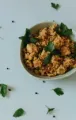 Bowl of seasoned rice or grain topped with green herbs on a white table