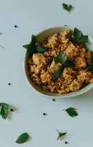 Bowl of seasoned rice or grain topped with green herbs on a white table
