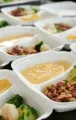Meal-prep trays with vegetables, beans, and yellow sauce arranged in rows on a table