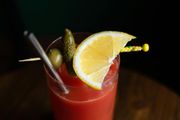 Red cocktail with lemon wedge, olives, and a stirrer in a glass against a dark background