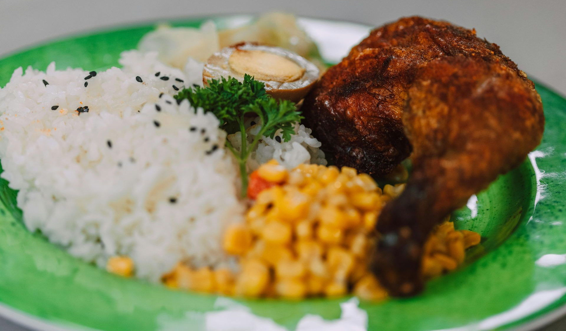 Plate of rice with fried chicken, corn, and garnish on a green tray