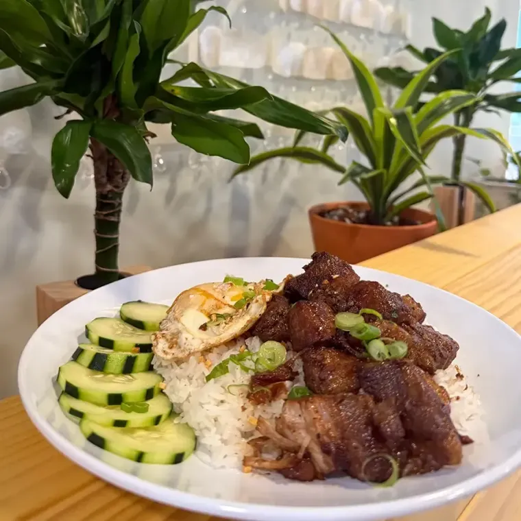 Plate of rice with braised meat, vegetables, and greens on a wooden table