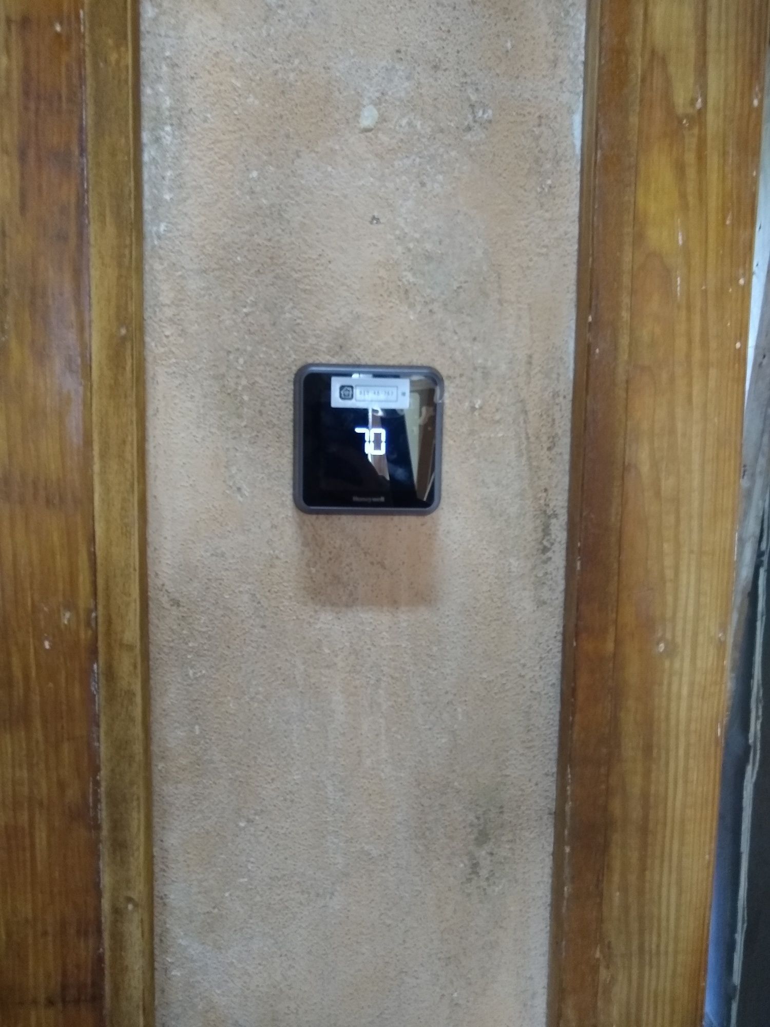 A thermostat is hanging on a wall next to a wooden door.