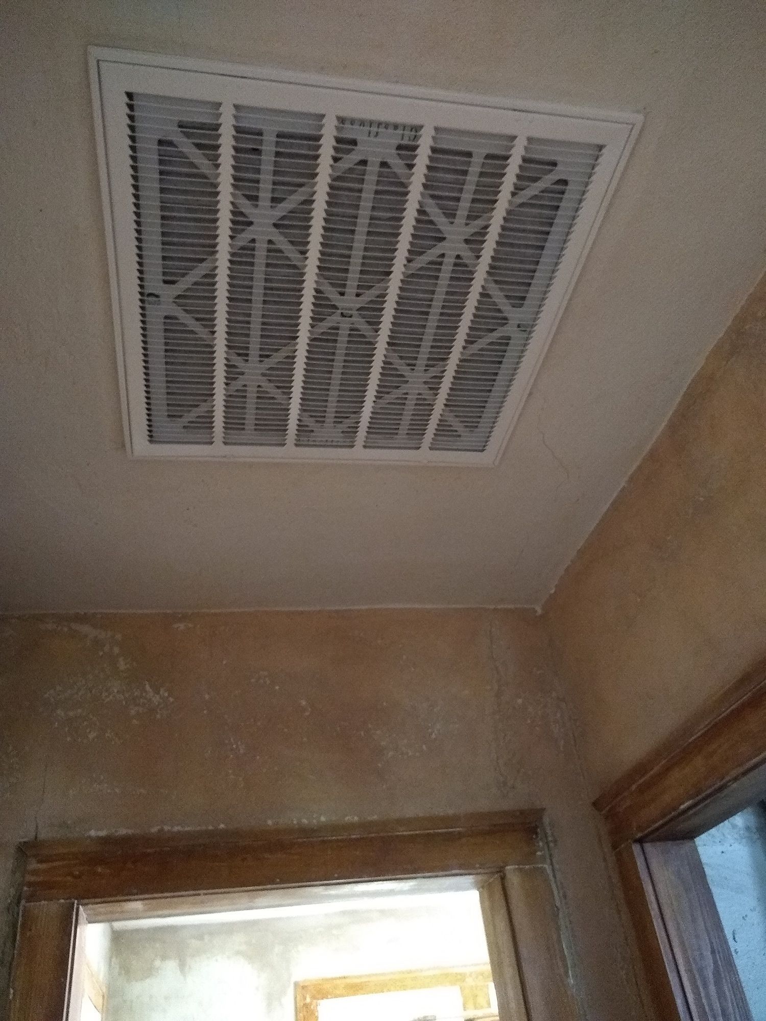 A white air vent is hanging from the ceiling of a room.