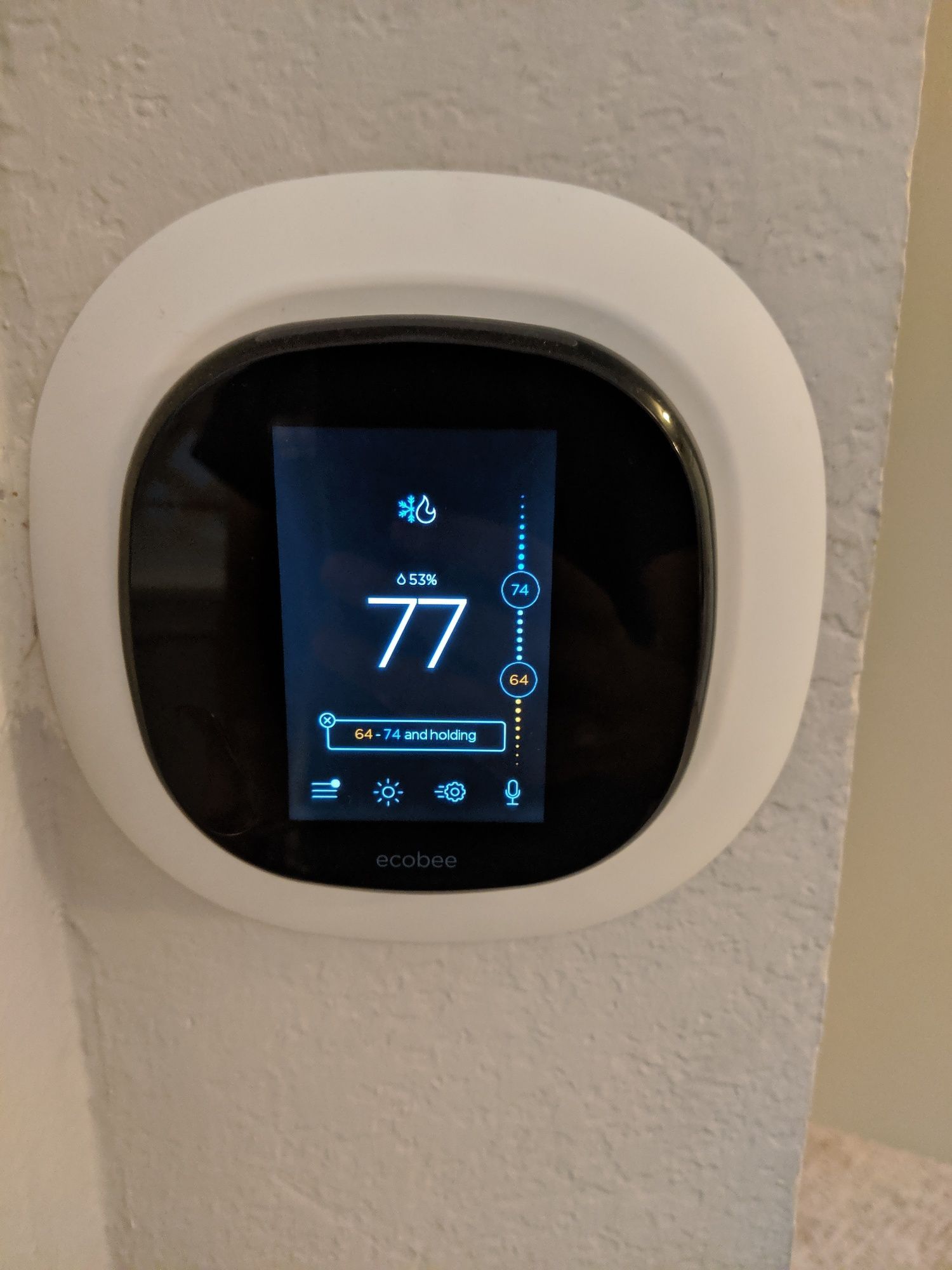 A thermostat is hanging on a wall and the temperature is 77 degrees fahrenheit.