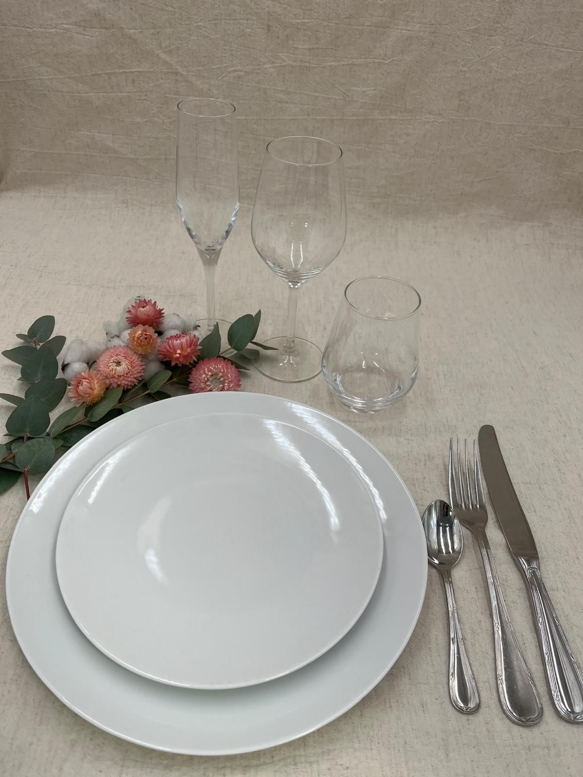 Élégante table dressée avec assiettes blanches, couverts, verres et fleurs roses sur une nappe beige