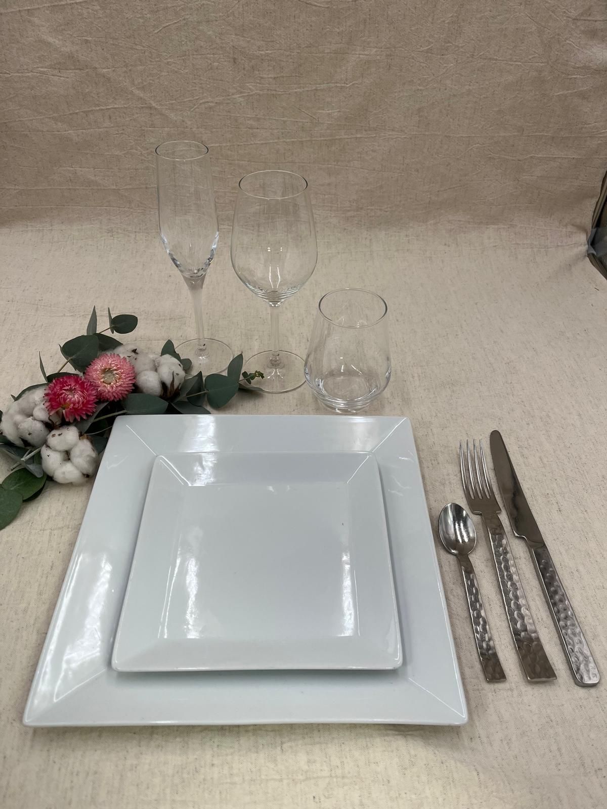 Élégante table dressée avec assiettes blanches, verres, couverts et centre de table floral rose sur une nappe beige
