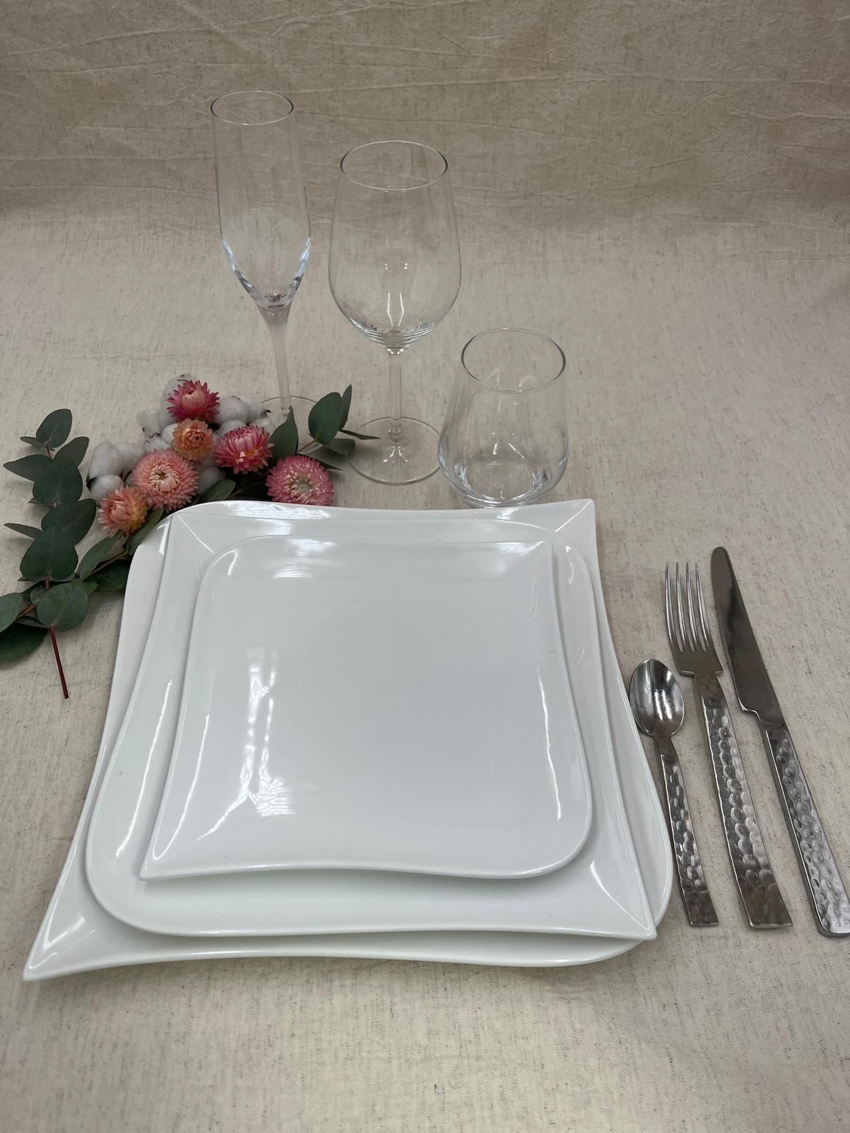 Élégante table dressée avec assiettes, verres et couverts blancs, et décor floral rose sur une nappe beige
