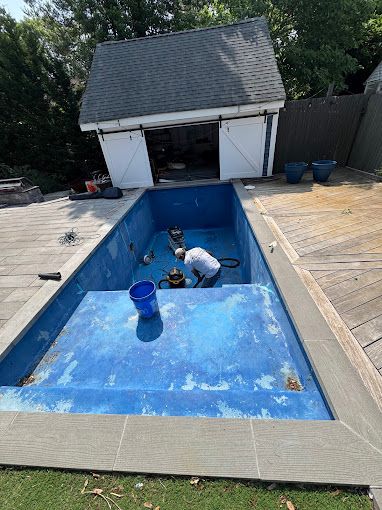 Man cleaning an empty blue swimming pool with a shed in the background