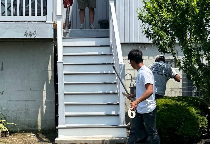 Three people painting white steps of a house. One is holding a paintbrush and tape, others in the background