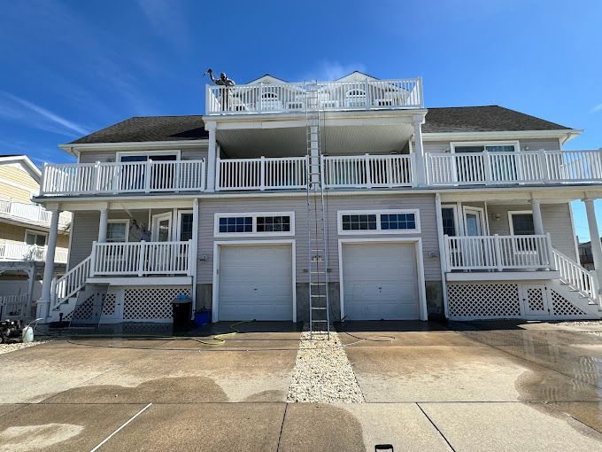 White beach house with two garage doors, balconies, and a ladder under a clear blue sky