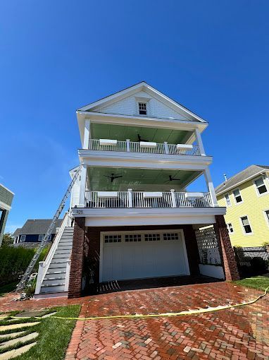 White house with brick garage and two-story balconies, set on brick driveway against a blue sky