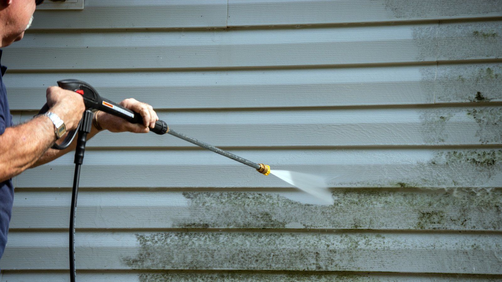 a person cleaning house siding with a pressure washer