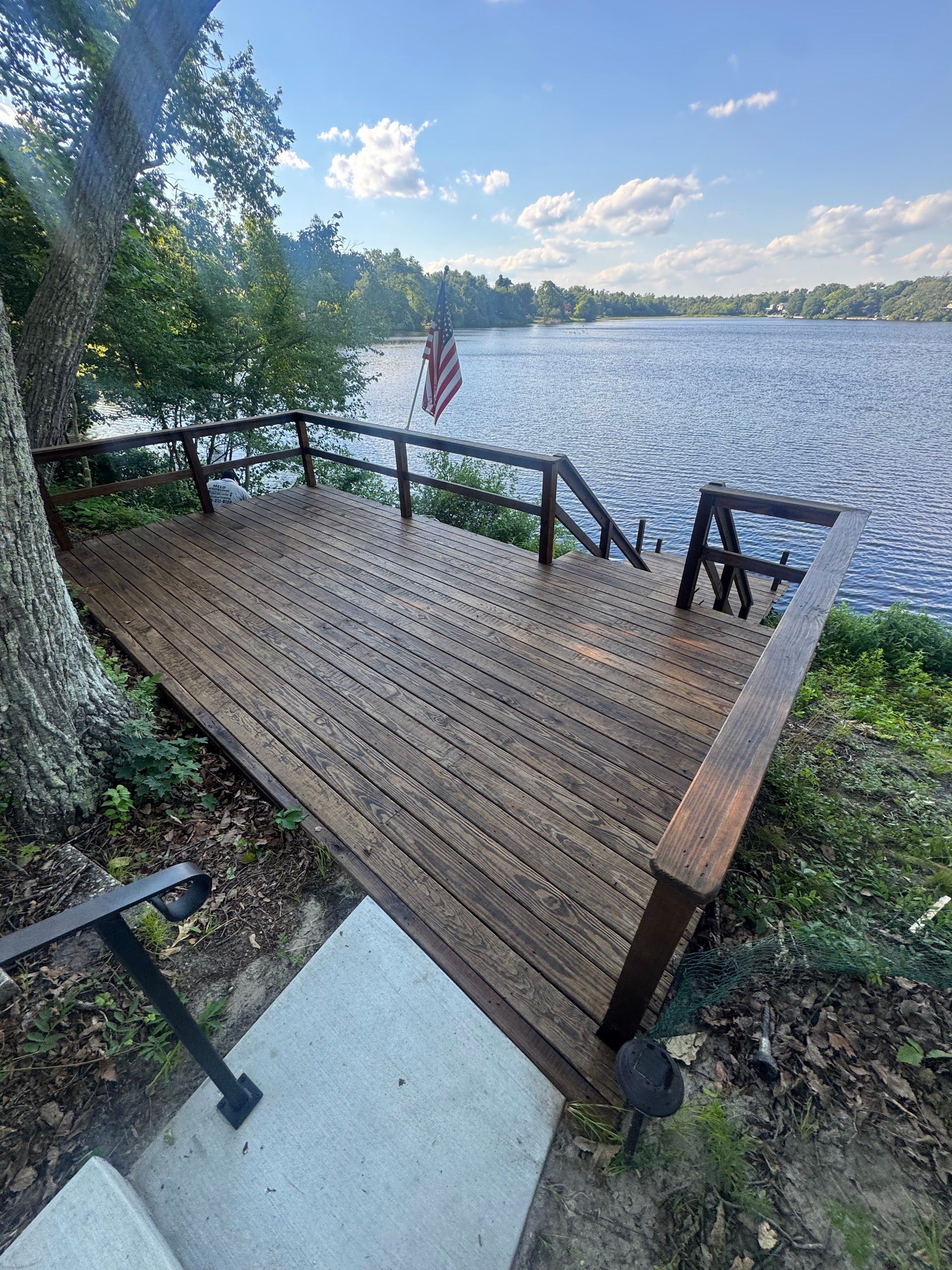 Wooden lakeside deck with railing, stairs, and an American flag overlooking calm water