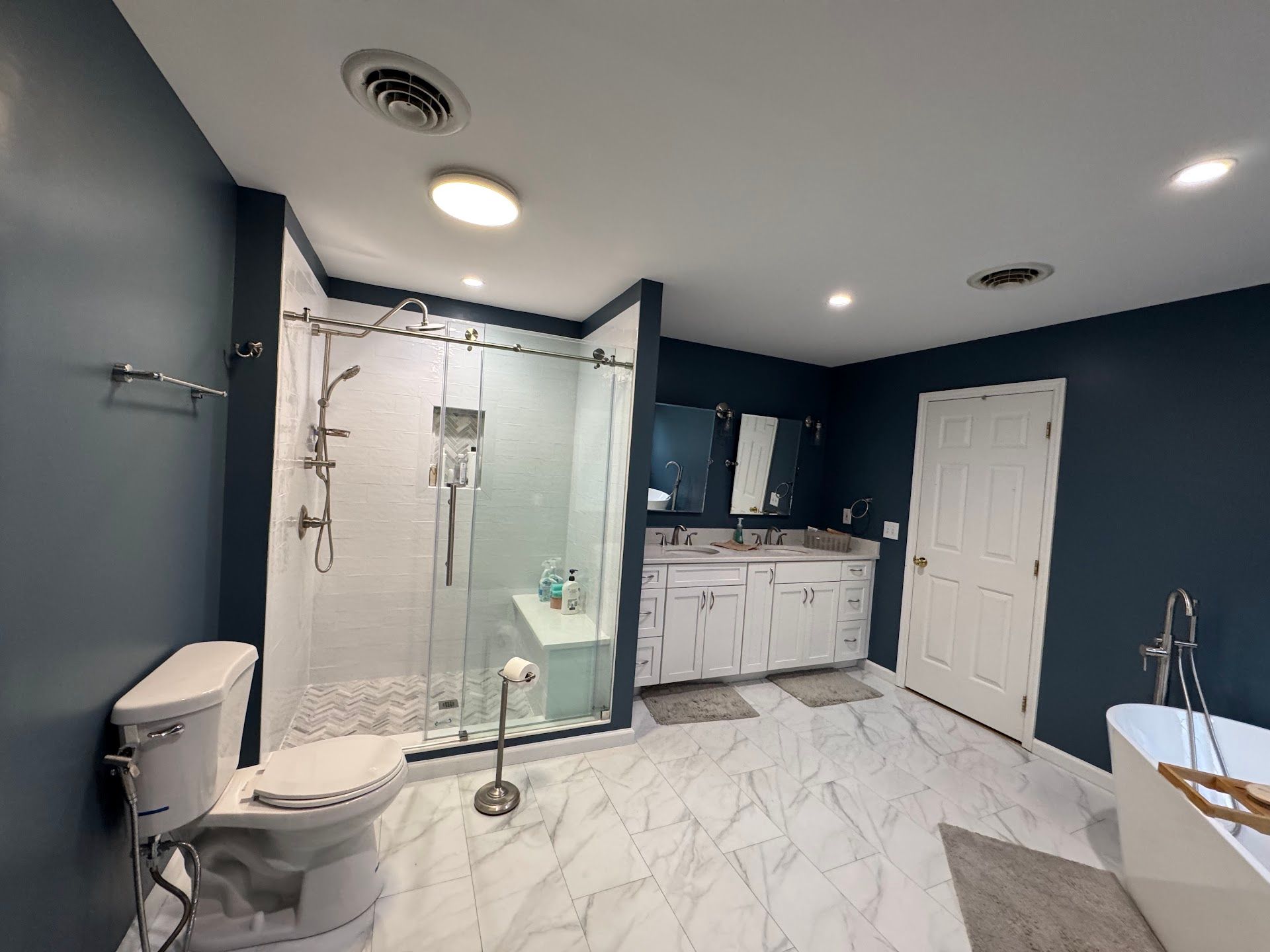 Modern bathroom with glass shower, toilet, vanity, and white marble tile floor