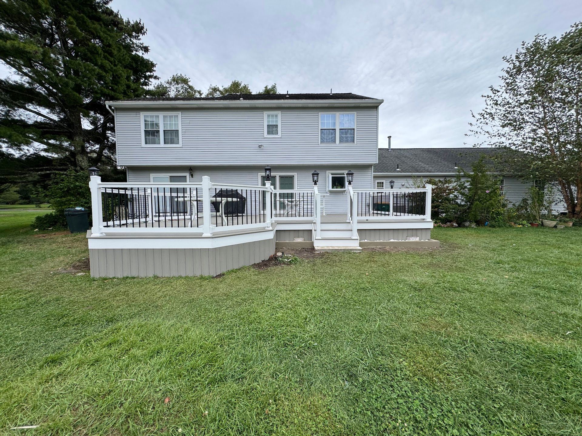 Two-story gray house with a white wraparound porch and green lawn under overcast skies