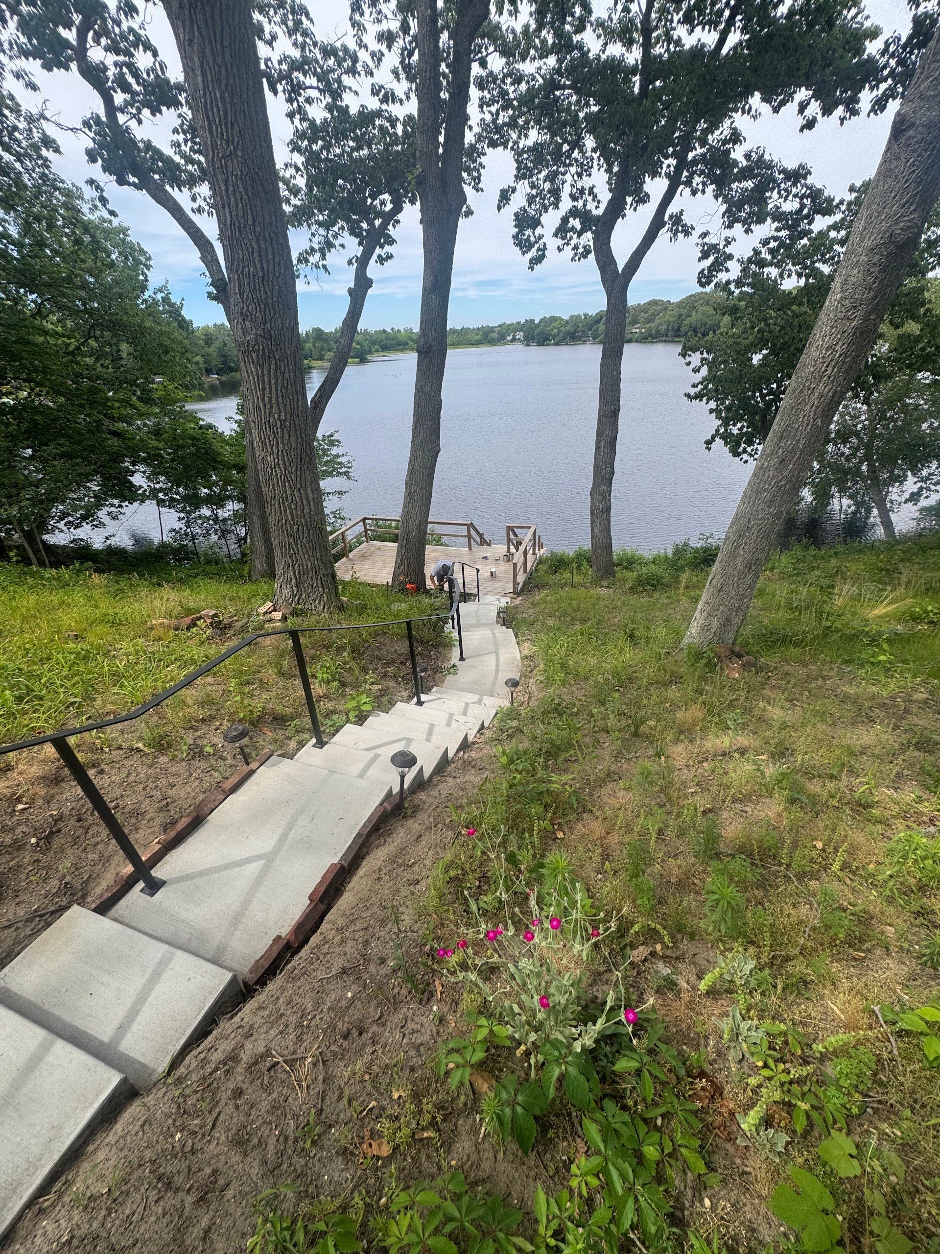 Concrete path through grassy trees leading to a lake with people at the water’s edge
