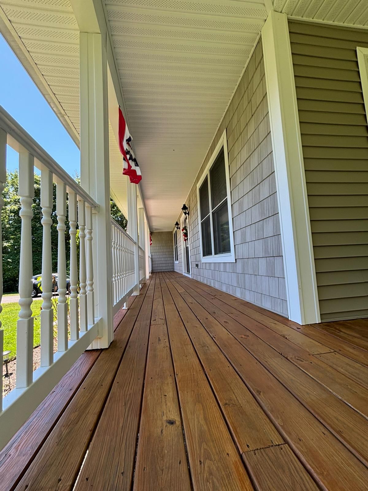 Wooden porch walkway with white railing and green siding, viewed in strong sunlight